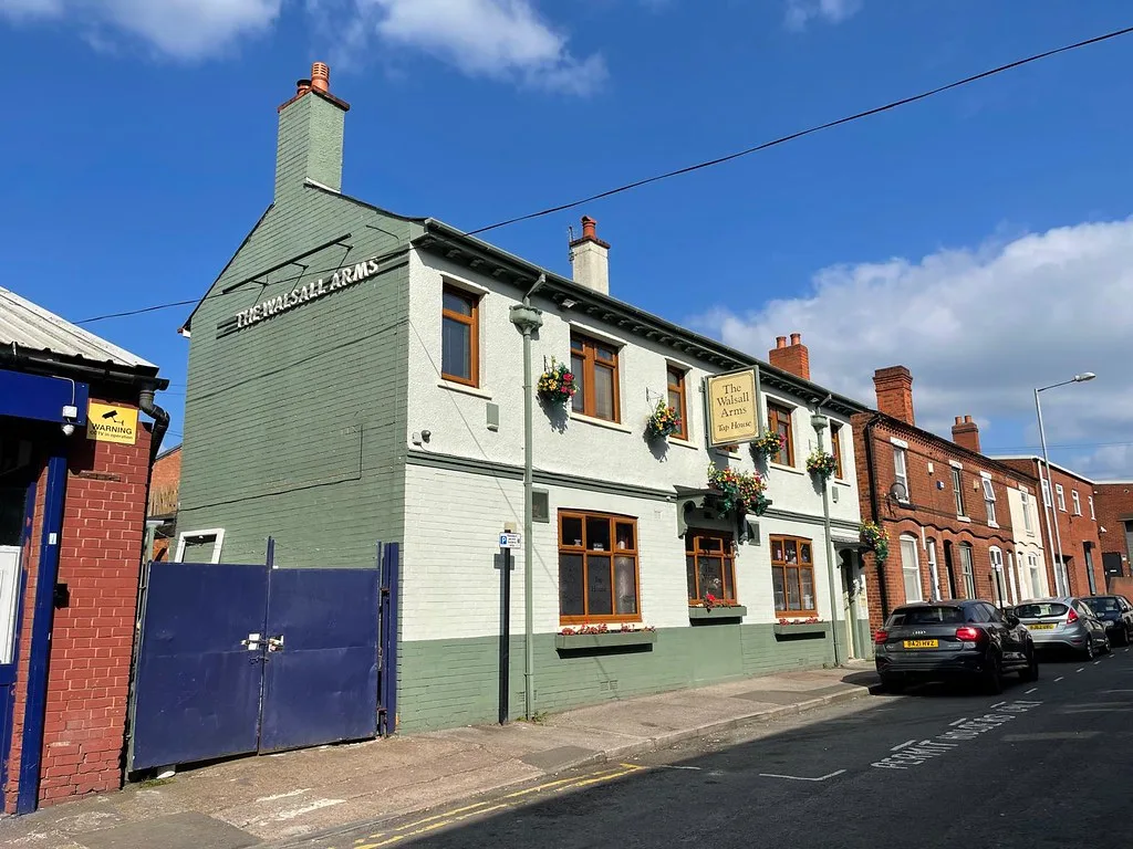 The Walsall Arms, a green and white painted pub with hanging baskets on a terraced back street