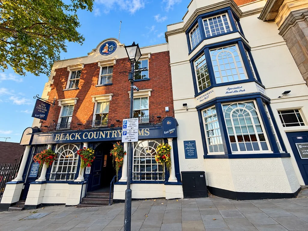 The Black Country Arms in Walsall, a red-brick and cream-painted pub with hanging baskets, steps up to the door and a lamp post outside