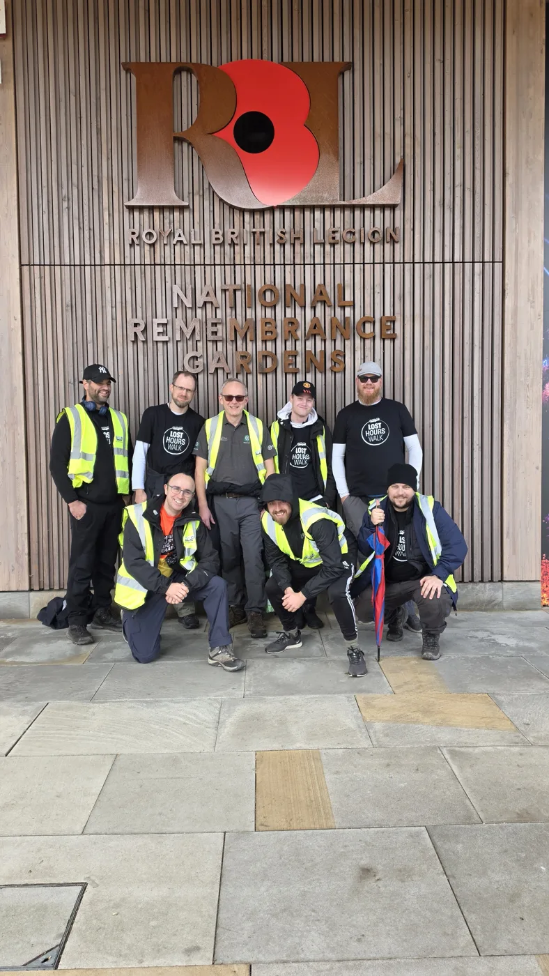 Nine walkers, some in Lost Hours Walk T-shirts and high-visibility vests, in front of the Royal British Legion National Remembrance Gardens sign
